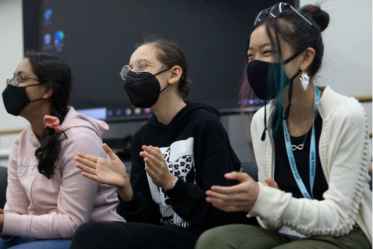 Three teenage girls laughing and applauding, wearing face masks