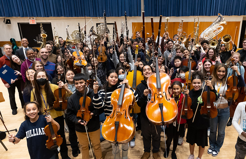 Group photo of smiling MAP students and teachers with instruments in the air